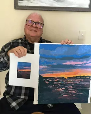 Customer holding a completed custom sunset paint by numbers beside the original photo