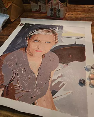 Custom portrait painting of a smiling woman with paint pots beside the canvas
