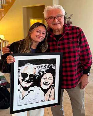 Grandfather and granddaughter holding a framed custom paint by numbers portrait together