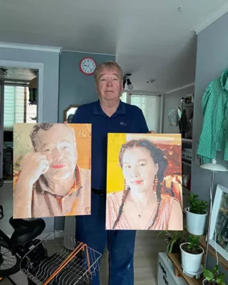 Man holding two finished custom paint by numbers portraits of a man and woman