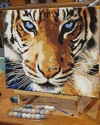 Striking finished paint by numbers close-up of a tiger staring forward with icy blue eyes, bold stripes, and richly layered golden fur