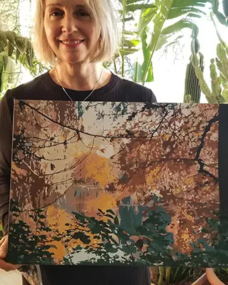 Woman holding a custom paint by numbers artwork of a colorful woodland landscape